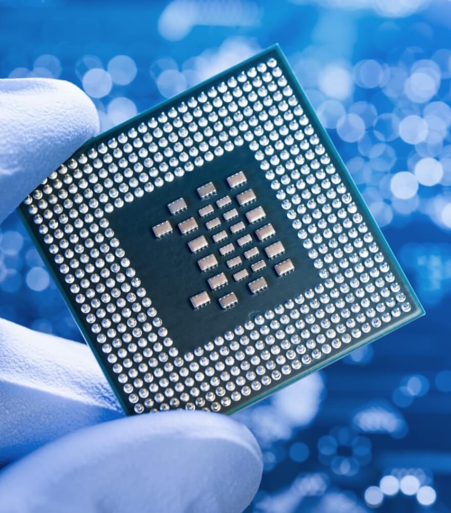 Close-up of a gloved hand holding a microchip with a blurred blue background.