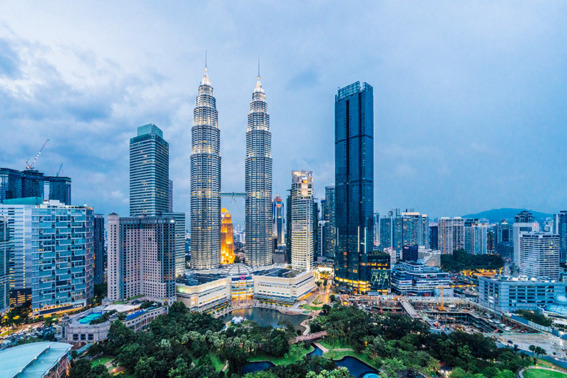 Aerial view of Kuala Lumpur skyline with the Petronas Twin Towers and surrounding skyscrapers during twilight. 