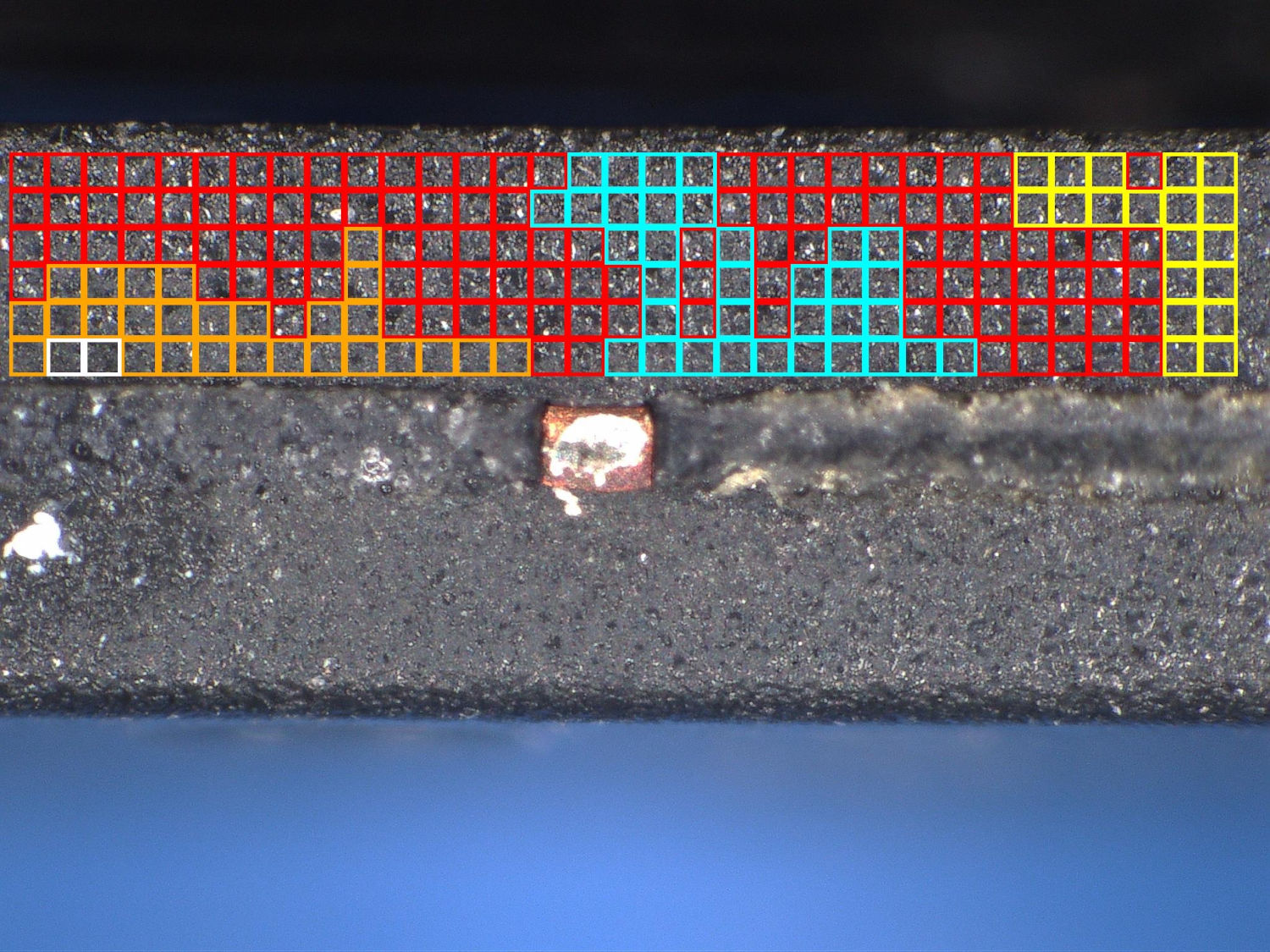 A close-up image showing a rectangular microchip with the top layer revealing a grid pattern of red, blue, and yellow squares to show color differences.