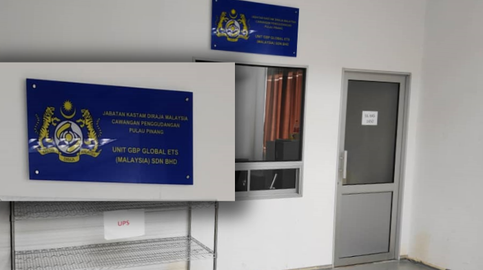 A room with a blue signboard that reads 'Jabatan Kastam Diraja Malaysia Cawangan Pengurangan Pulau Pinang Unit GLP Global ETS (Malaysia) Sdn Bhd' and a metal rack below it. To the right is a closed door.