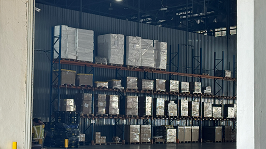 Interior of a warehouse with tall metal shelves stacked with large, wrapped pallets of electronic components.