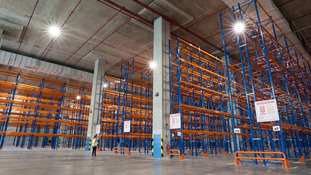 Interior of a large semiconductor warehouse with empty blue and orange industrial shelving units and a high ceiling with bright lights.